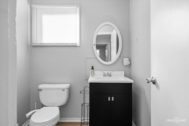 half bath featuring baseboards, vanity, and toilet