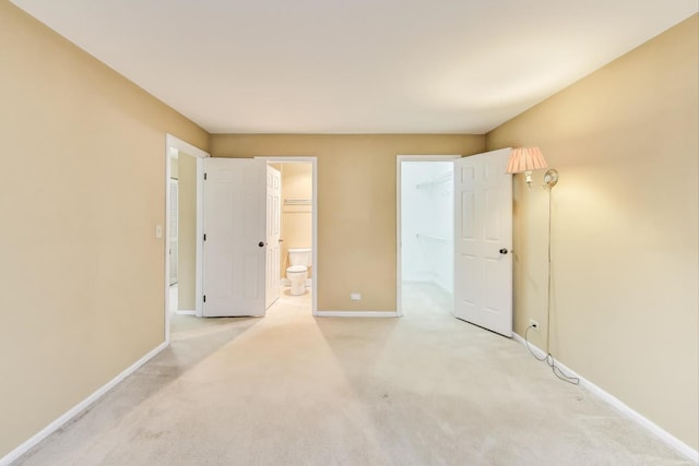 unfurnished bedroom featuring ensuite bathroom, a walk in closet, light colored carpet, and baseboards