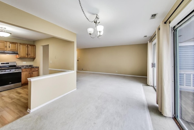 kitchen featuring baseboards, light colored carpet, gas range, decorative light fixtures, and under cabinet range hood