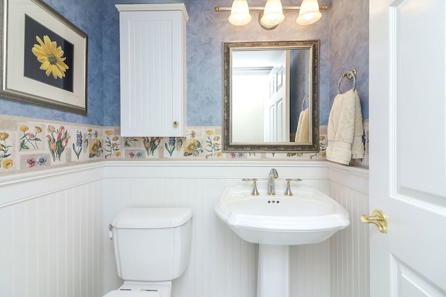 half bath with toilet, wainscoting, and wallpapered walls