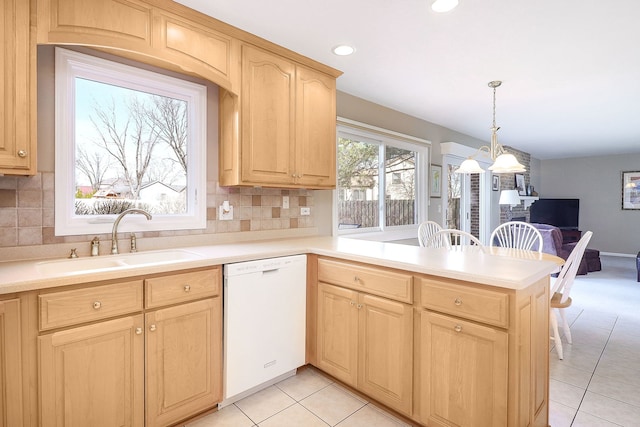 kitchen with light brown cabinets, a sink, a peninsula, light countertops, and dishwasher