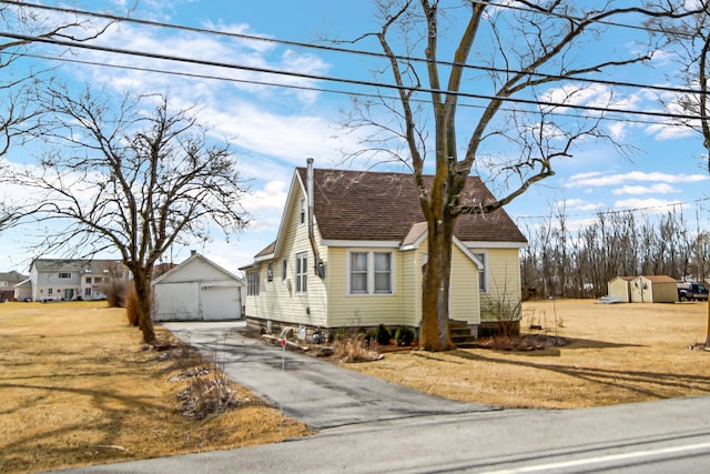 view of front of property featuring an outbuilding, a shingled roof, a garage, driveway, and a front lawn