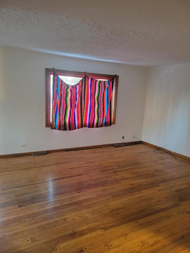 empty room featuring hardwood / wood-style flooring, baseboards, and a textured ceiling