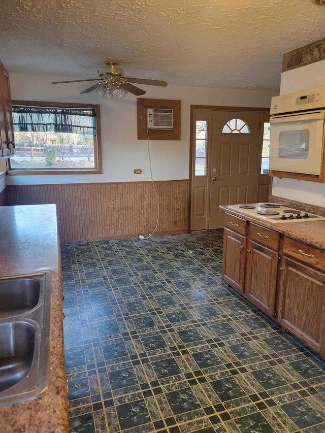 kitchen with an AC wall unit, wainscoting, a sink, a textured ceiling, and white appliances