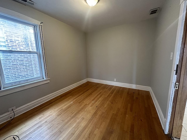 empty room with wood-type flooring, visible vents, and baseboards