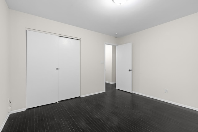 unfurnished bedroom with a closet, dark wood finished floors, and baseboards