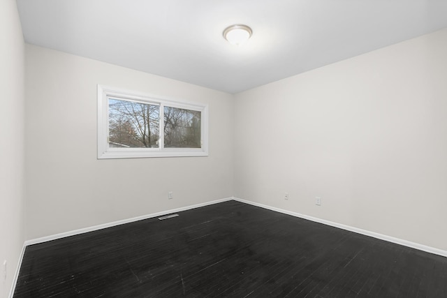 spare room with dark wood-type flooring, visible vents, and baseboards