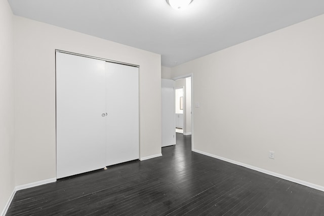 unfurnished bedroom with dark wood-style floors, a closet, and baseboards