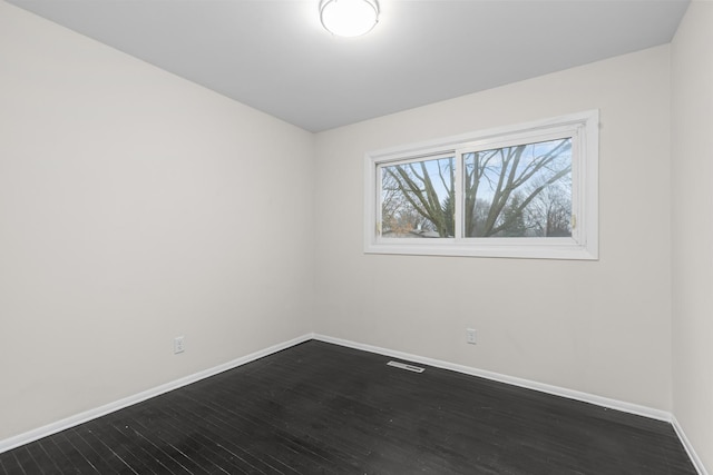 empty room featuring dark wood-style flooring, visible vents, and baseboards