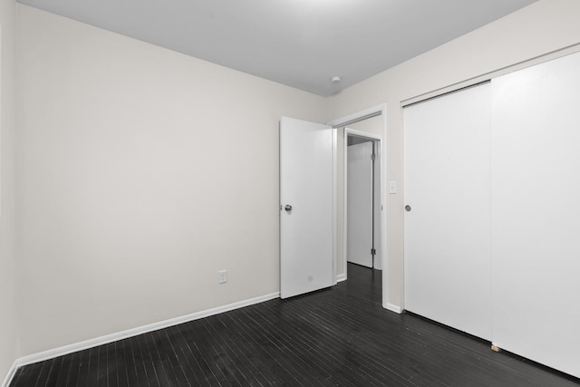 unfurnished bedroom featuring a closet, dark wood finished floors, and baseboards