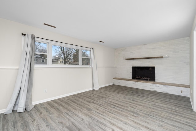 unfurnished living room featuring a brick fireplace, visible vents, baseboards, and wood finished floors