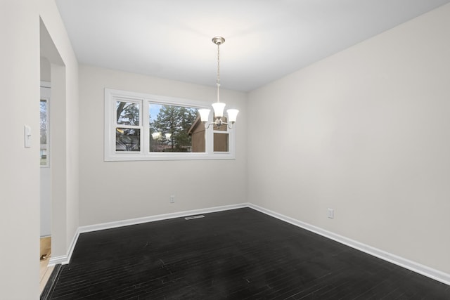 unfurnished room with dark wood-style flooring, a notable chandelier, and baseboards