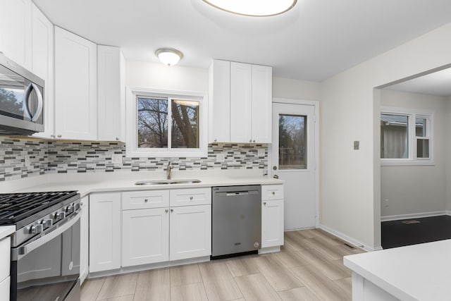 kitchen featuring stainless steel appliances, light countertops, backsplash, white cabinetry, and a sink