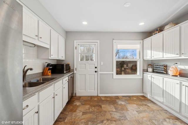 kitchen with stainless steel appliances, decorative backsplash, white cabinetry, a sink, and baseboards