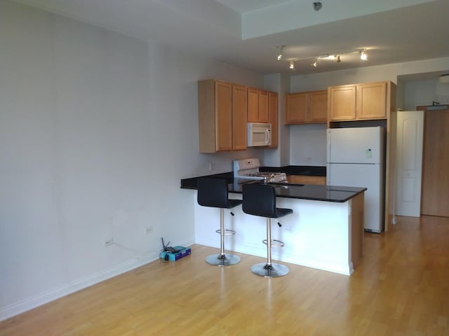 kitchen with white appliances, dark countertops, a peninsula, and light wood-style flooring