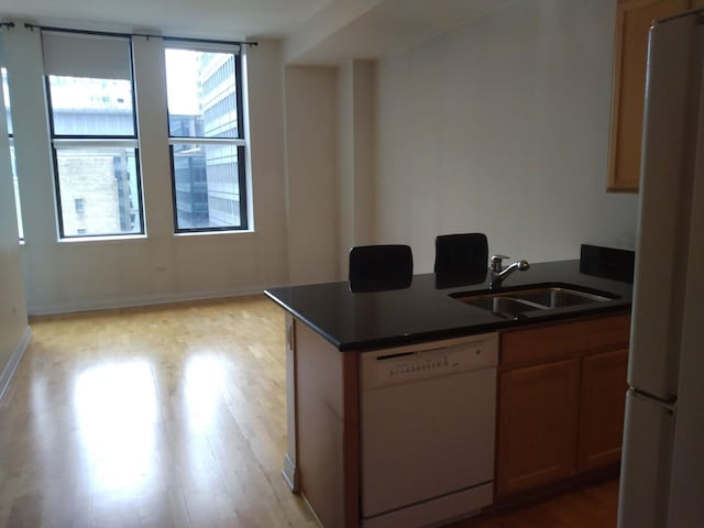 kitchen featuring white appliances, dark countertops, light wood finished floors, and a sink