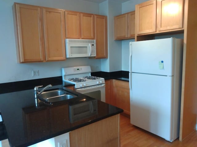 kitchen with dark countertops, white appliances, and a sink