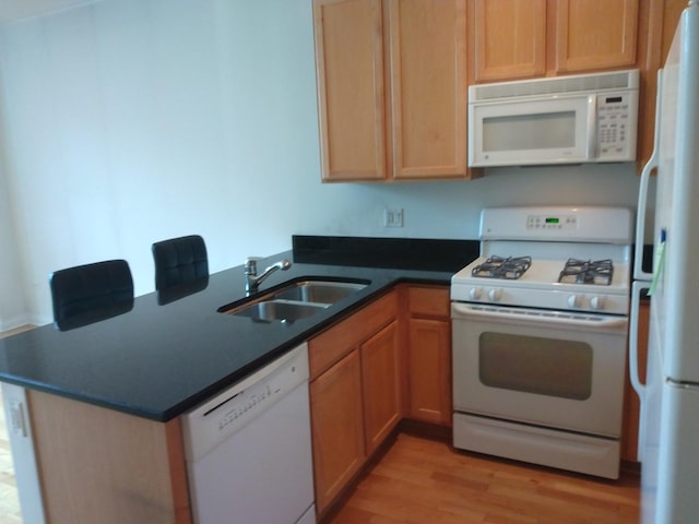 kitchen featuring dark countertops, light wood-type flooring, a peninsula, white appliances, and a sink