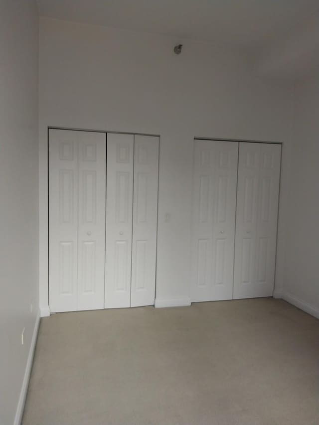 unfurnished bedroom with carpet, baseboards, and two closets