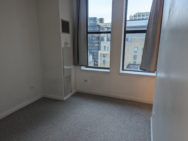 unfurnished room featuring a city view, visible vents, baseboards, and carpet floors