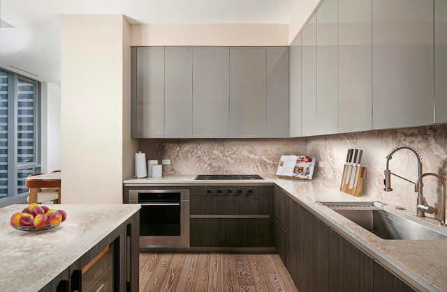 kitchen with a sink, stainless steel oven, decorative backsplash, black stovetop, and modern cabinets