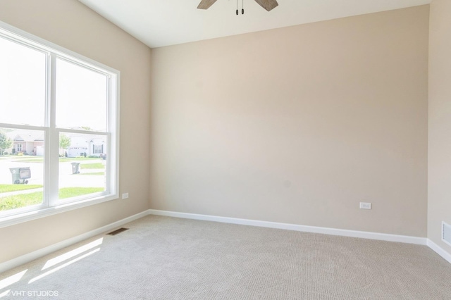 spare room featuring light carpet, a ceiling fan, visible vents, and baseboards