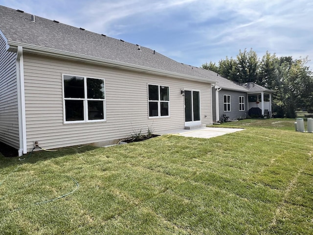 back of property featuring a shingled roof, a patio, and a yard