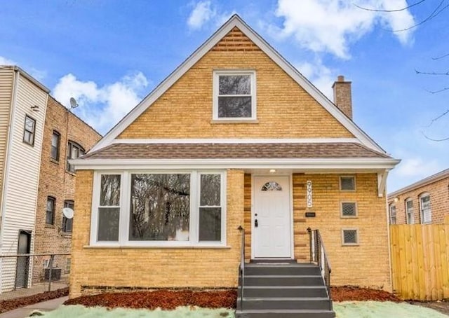 bungalow-style house with a chimney, fence, and brick siding