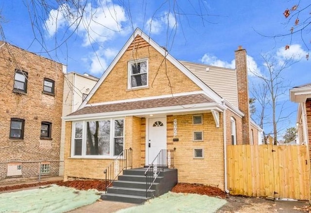 view of front of house with roof with shingles, brick siding, a chimney, and fence