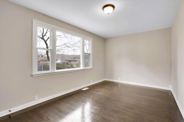 empty room featuring dark wood-style floors, visible vents, and baseboards