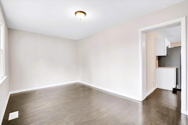 spare room with dark wood finished floors, visible vents, and baseboards