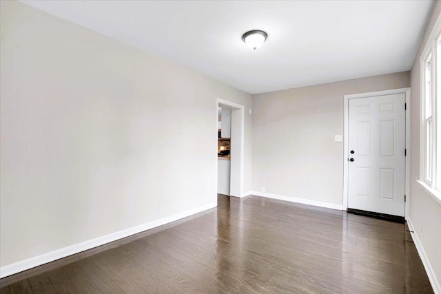 spare room featuring baseboards and dark wood-type flooring