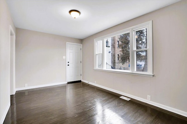 empty room featuring dark wood-style floors, visible vents, and baseboards