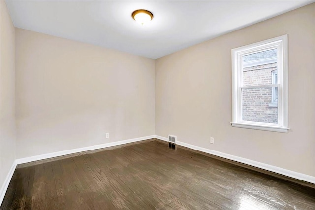 unfurnished room with dark wood-type flooring, visible vents, and baseboards