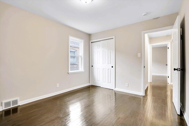 unfurnished bedroom featuring baseboards, a closet, visible vents, and dark wood-type flooring