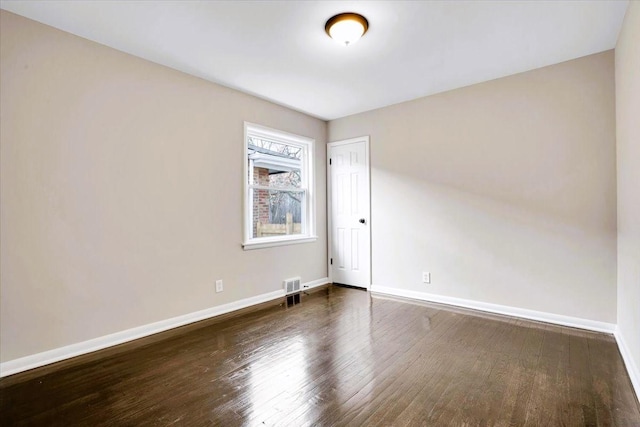 spare room with visible vents, baseboards, and dark wood-type flooring