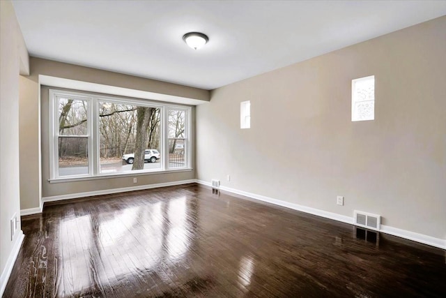 spare room with dark wood-style flooring, visible vents, and baseboards