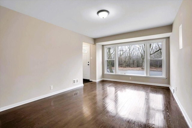 empty room with dark wood-type flooring, visible vents, and baseboards