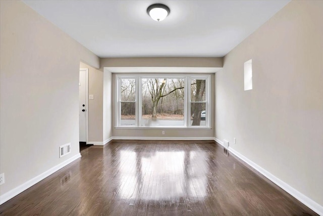 spare room with baseboards, visible vents, and dark wood-type flooring