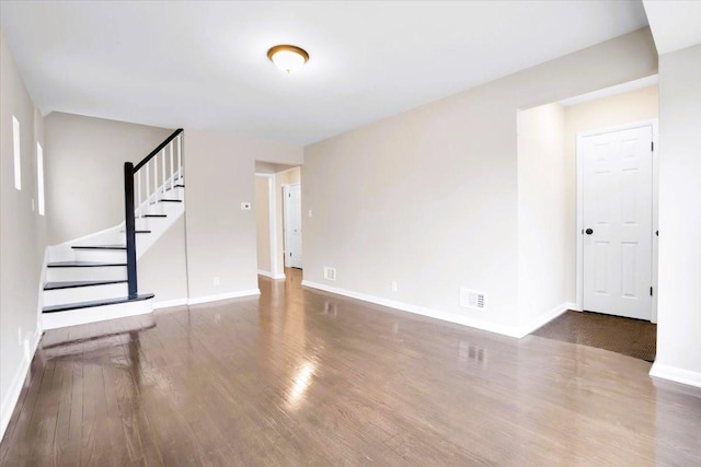 unfurnished living room featuring visible vents, stairway, baseboards, and wood finished floors