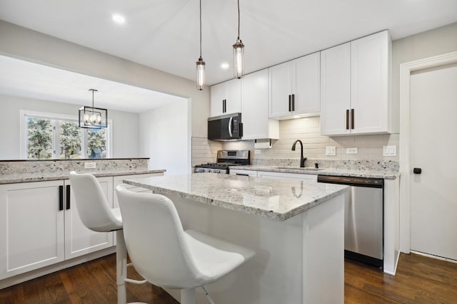 kitchen featuring a sink, a kitchen island, tasteful backsplash, dark wood-style floors, and appliances with stainless steel finishes