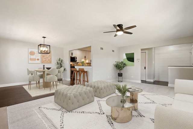 living area with ceiling fan with notable chandelier, visible vents, wood finished floors, and baseboards