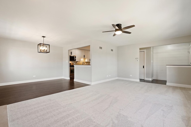 unfurnished living room featuring visible vents, baseboards, carpet flooring, and ceiling fan with notable chandelier