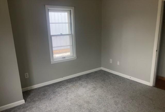 empty room featuring baseboards and dark colored carpet