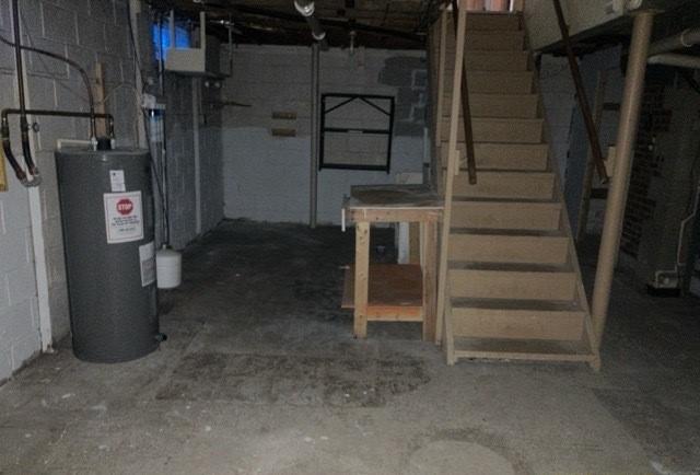 unfinished basement featuring concrete block wall, water heater, and stairs