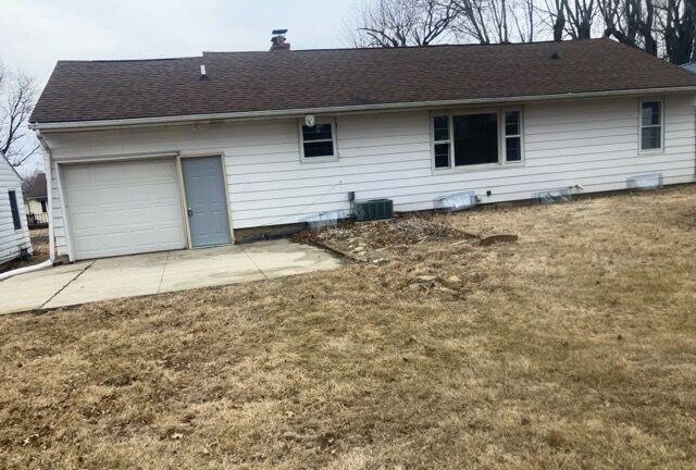 rear view of house with central AC unit, a lawn, concrete driveway, a chimney, and an attached garage