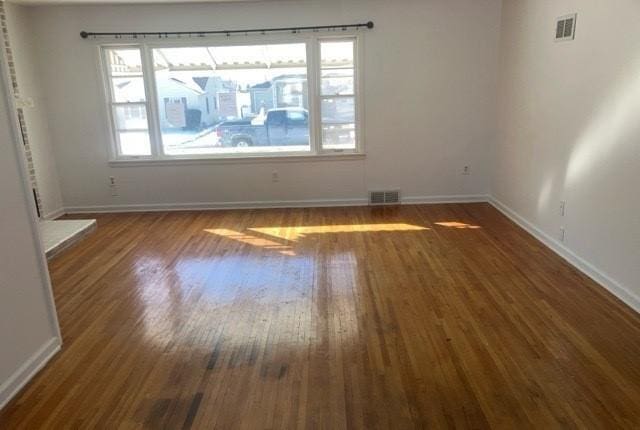 unfurnished room featuring baseboards, visible vents, and wood finished floors