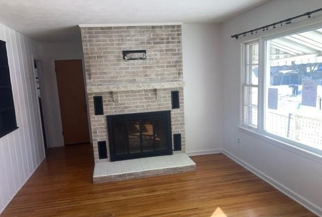 unfurnished living room featuring a brick fireplace, baseboards, and wood finished floors