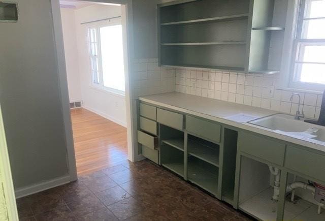 kitchen with open shelves, backsplash, a sink, and light countertops