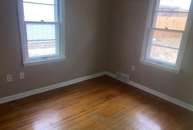 unfurnished room with baseboards, visible vents, and dark wood-style flooring